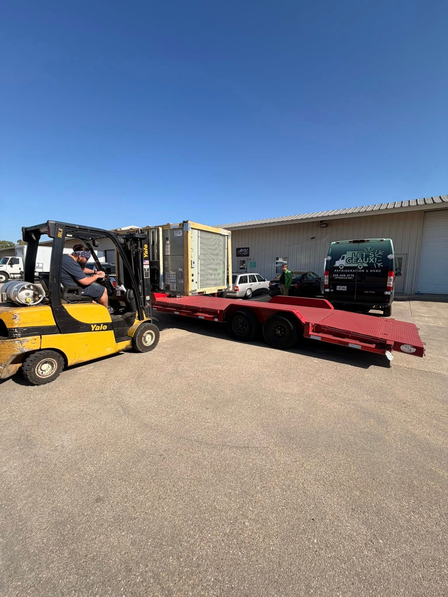 Forklift loading large HVAC or refrigeration equipment onto a trailer